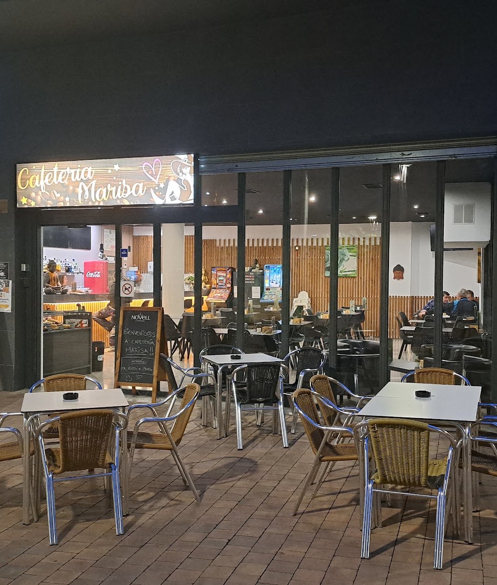 Façana de la Cafeteria Marisa de nit, amb el rètol lluminós i les taules de la terrassa
